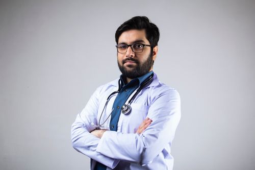 Free Portrait of a serious male doctor in a white coat with a stethoscope, arms crossed, studio background. Stock Photo