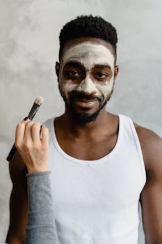 Black man with clay mask being applied as part of beauty and skincare routine.