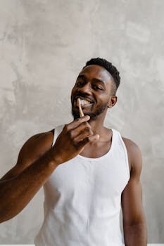 African American man in white tank top holding toothbrush and smiling, promoting oral hygiene.