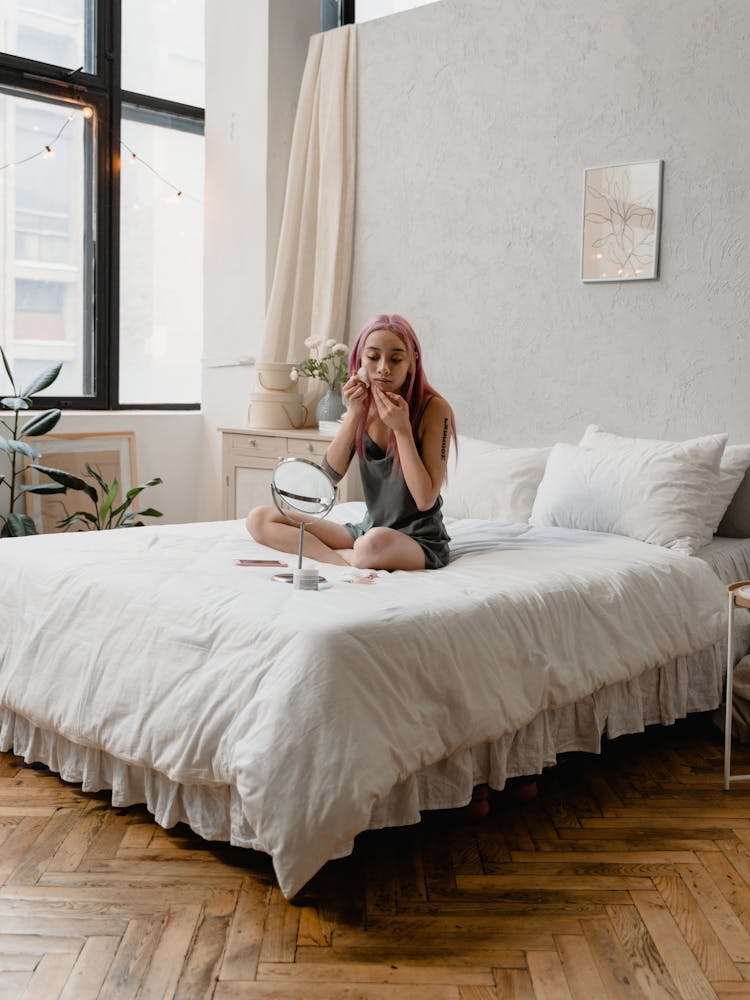 A Woman Peeling Her Face Mask While Sitting On The Bed