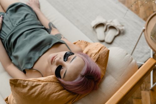 Free A woman with pink hair relaxes on a couch wearing under eye masks for skincare. Stock Photo