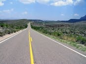 一条长长的开放道路穿过风景优美的沙漠景观，在明亮的蓝天下延伸