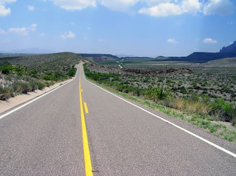 一条长长的开放道路穿过风景优美的沙漠景观，在明亮的蓝天下延伸