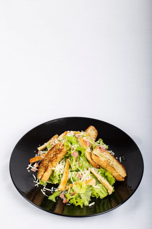Free Delicious Caesar salad topped with grilled chicken and cheese on a black plate, perfect for a healthy meal. Stock Photo