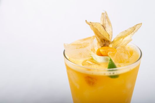 Close-up of a refreshing citrus drink with ice cubes and physalis garnish on a white background.