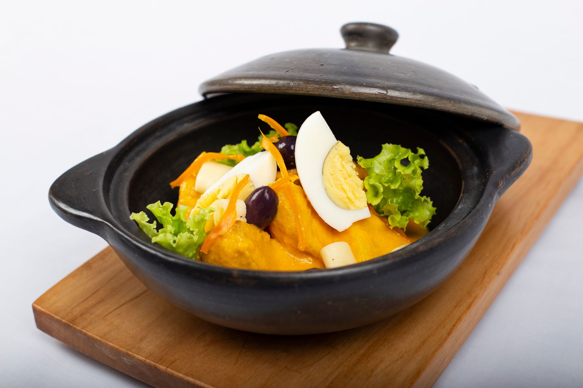 Delicious gourmet dish with eggs and greens in a black cast iron bowl on a wooden board.