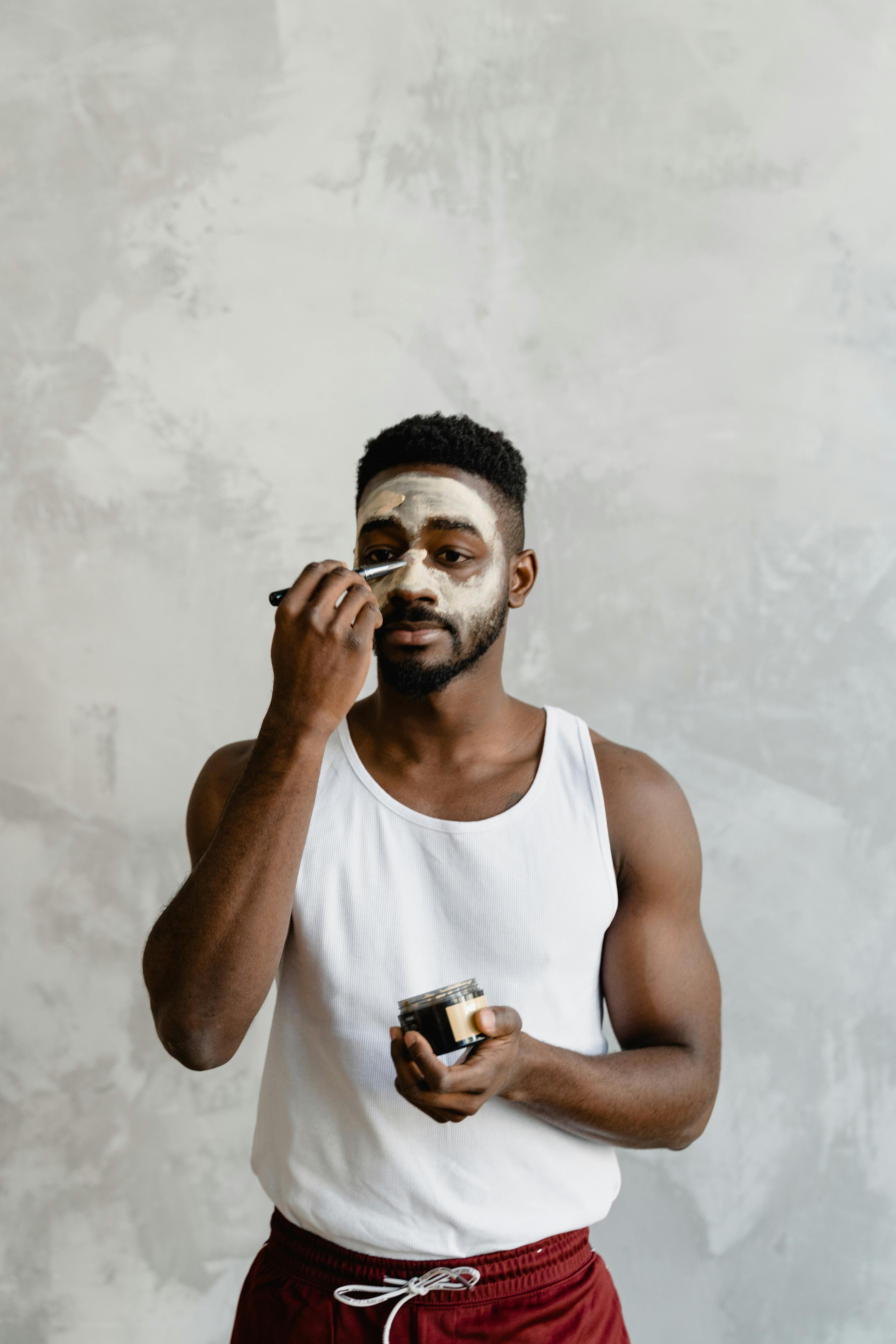 Young black man applying a clay mask indoors for skincare and self-care routine.