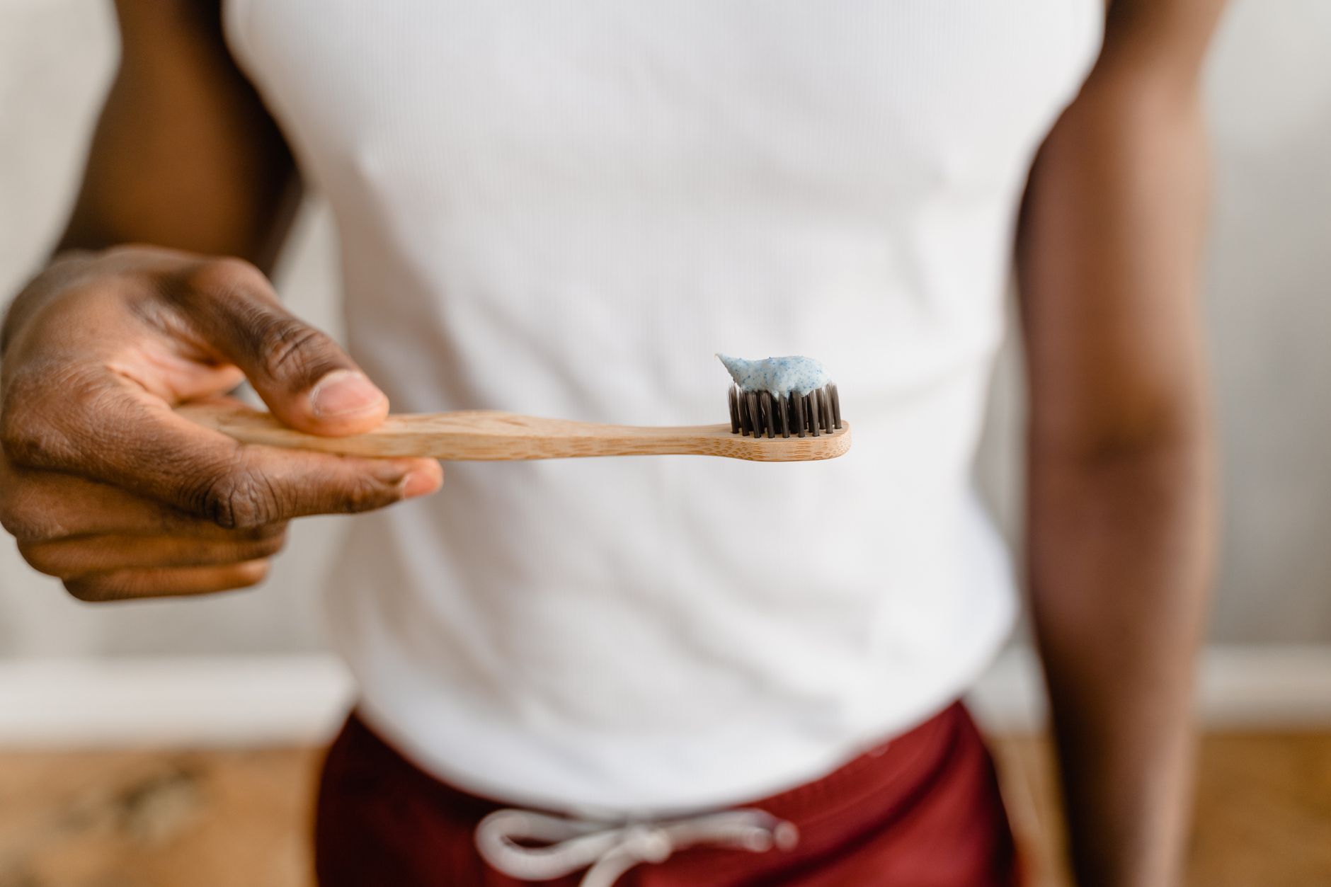 A person holding a bamboo toothbrush with a dab of toothpaste on the bristles