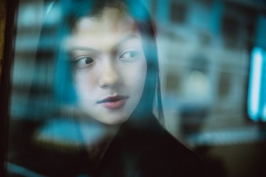 Through glass wall view of crop young ethnic female with makeup looking away in daytime