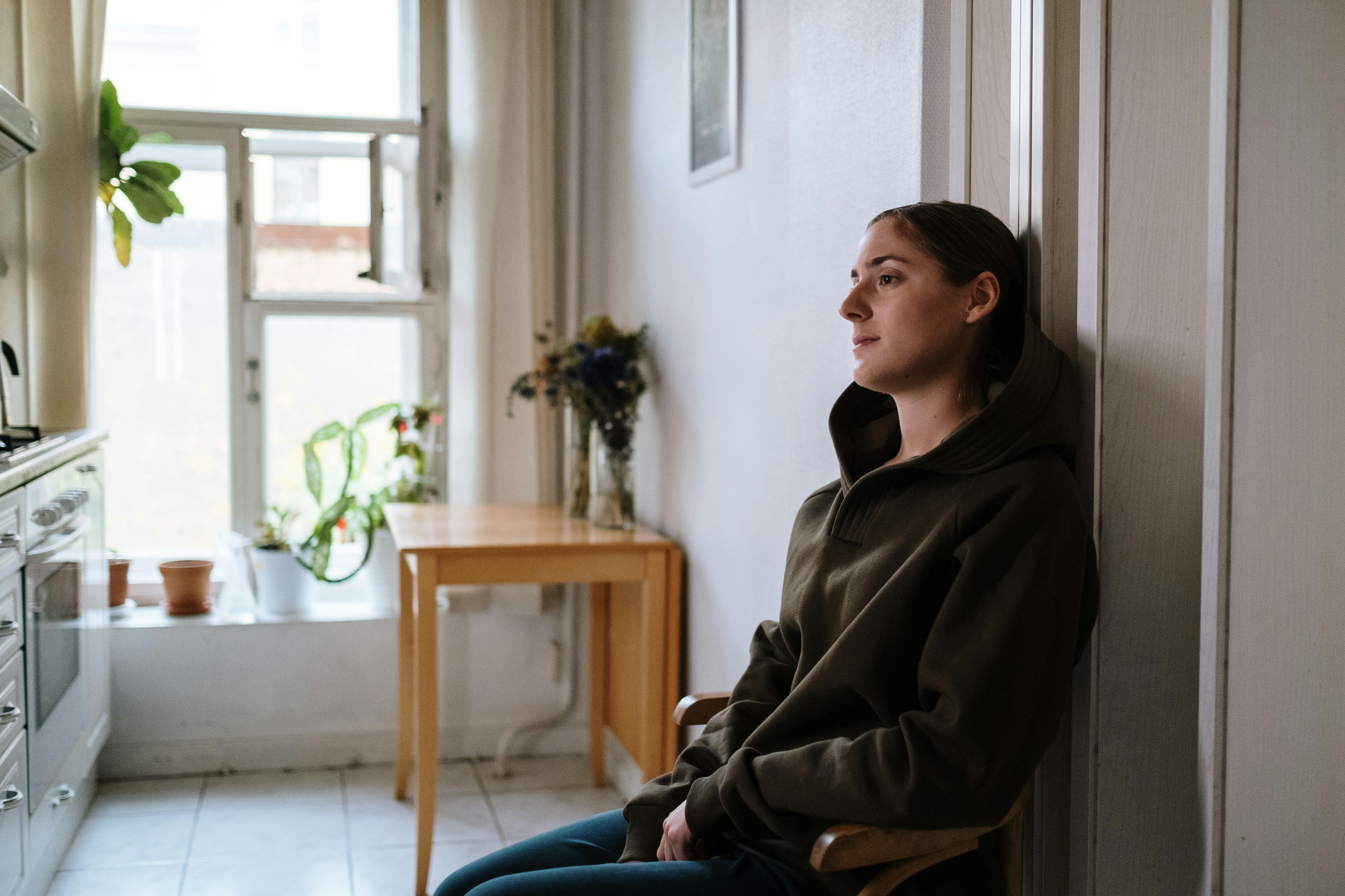 Image of a person sitting alone, looking out a window, conveying a sense of isolation and quiet struggle due to an invisible illness - what is chronic pain