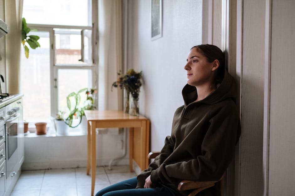 Image of a person sitting alone, looking out a window, conveying a sense of isolation and quiet struggle due to an invisible illness - what is chronic pain Image of a person sitting alone, looking out a window, conveying a sense of isolation and quiet struggle due to an invisible illness - what is chronic pain