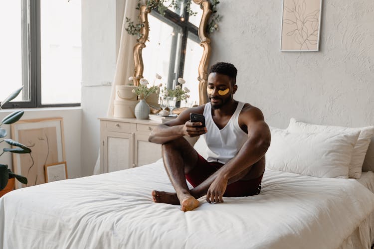 Man In White Sleeveless Shirt Sitting On White Bed