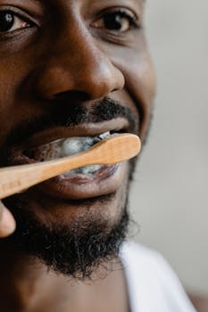 A close-up of a man using a bamboo toothbrush to brush his teeth indoors.