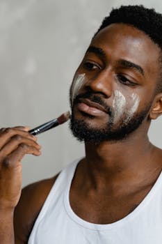 Close-up of an adult man applying face cream with a brush indoors.
