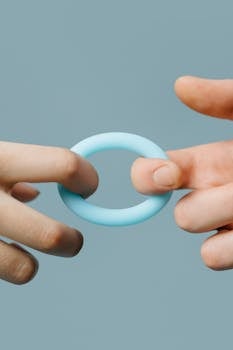 Detailed view of hands delicately holding a blue silicone ring against a neutral backdrop.
