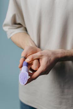 A person in a beige shirt holding a purple silicone finger vibrator in a close-up shot.
