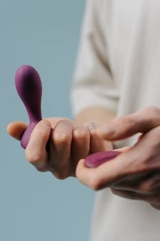 A hand holding a soft purple vibrator with a smooth texture against a light background.