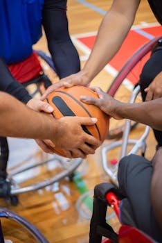 Close-up of hands holding basketball in wheelchair game, symbolizing team support and inclusivity.