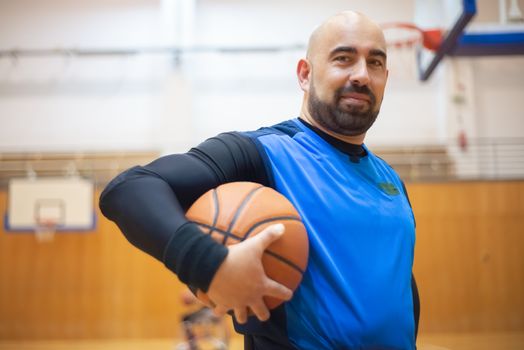 A middle-aged man confidently poses with a basketball in an indoor gym setting.