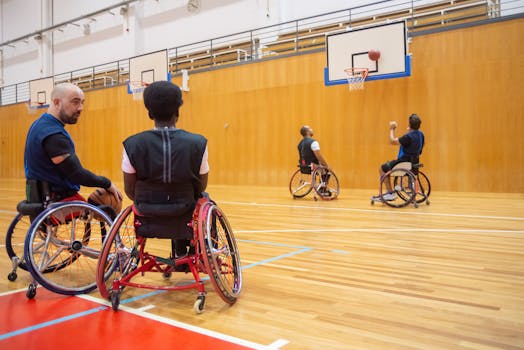 Four men in wheelchairs playing basketball indoors, promoting inclusivity.