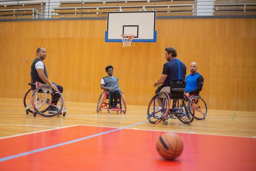 Four men in wheelchairs playing basketball indoors, focusing on adaptive sports and teamwork.