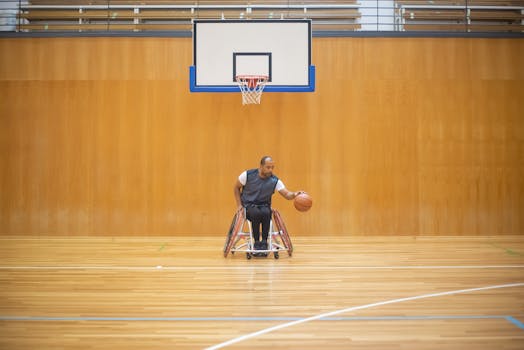 Man in a wheelchair dribbling a basketball on an indoor court, showcasing athleticism and determination.