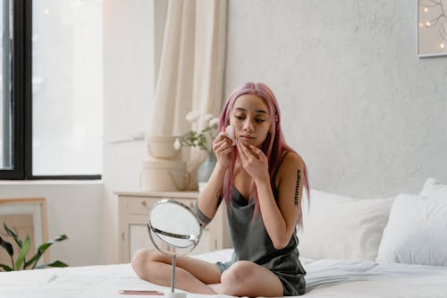 Free Woman Doing Skincare Routine while Sitting on Bed Stock Photo