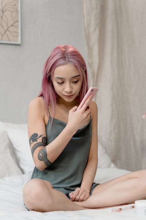 Woman Sitting on Bed while Using a Cellphone