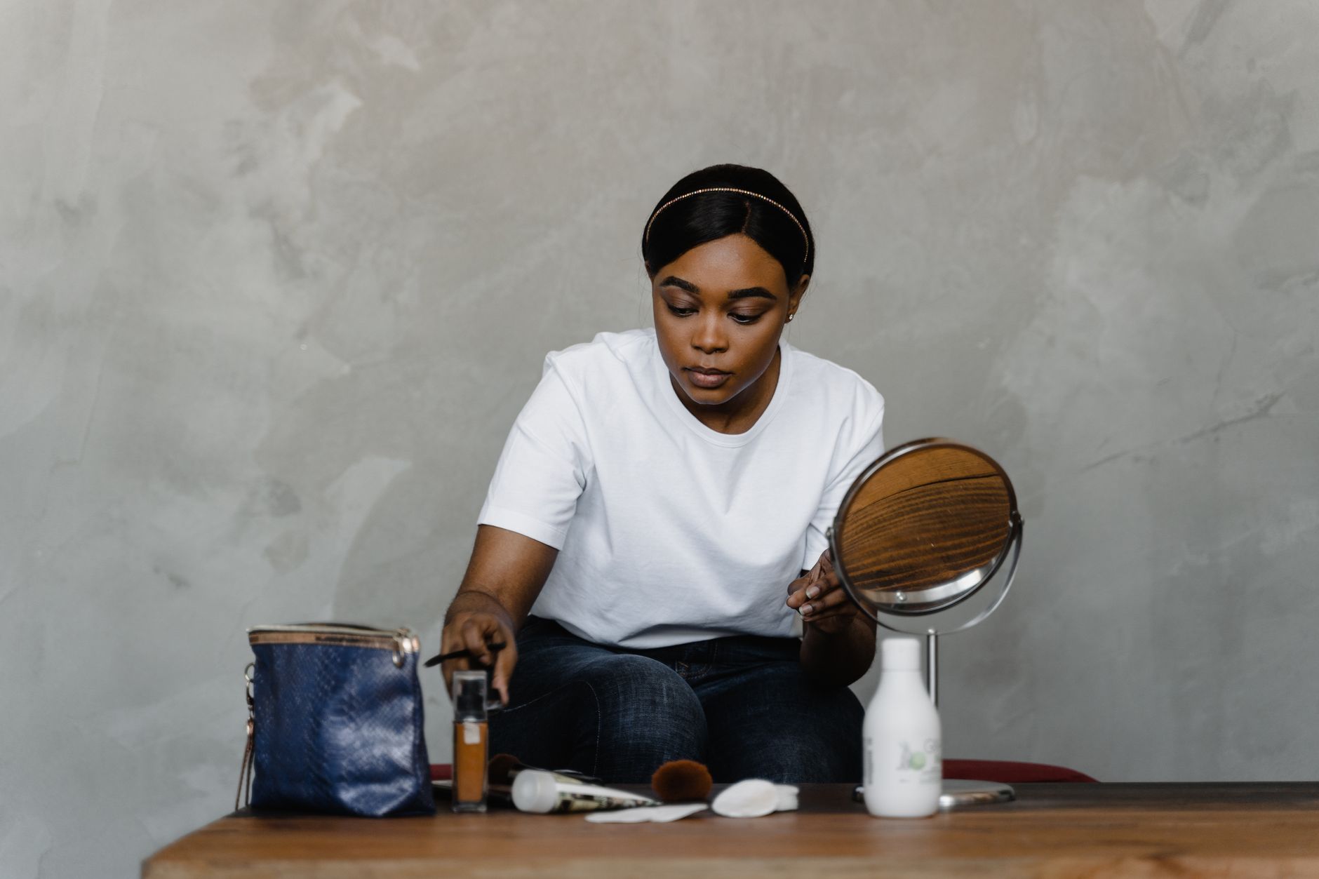 African American woman applying makeup indoors with a mirror and beauty products on a table.
