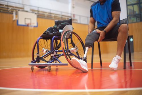 Free Adaptive sports athlete adjusting prosthetic leg on a basketball court, epitomizing resilience and inclusivity. Stock Photo