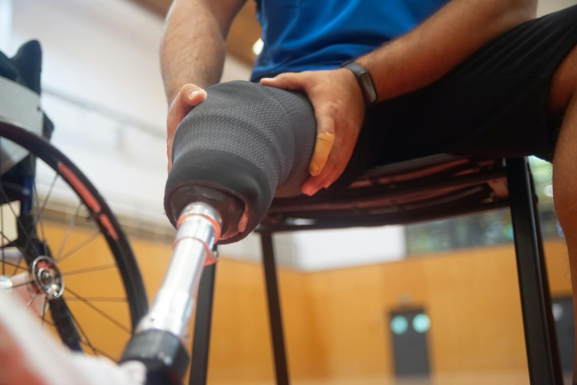 Close-up of a man adjusting his prosthetic leg while sitting indoors, emphasizing disability support.