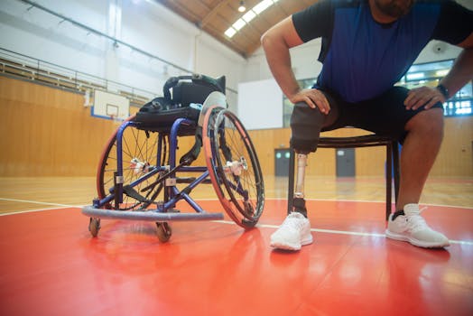 A focused shot of an adaptive athlete with a prosthetic leg taking a break on a basketball court indoors.