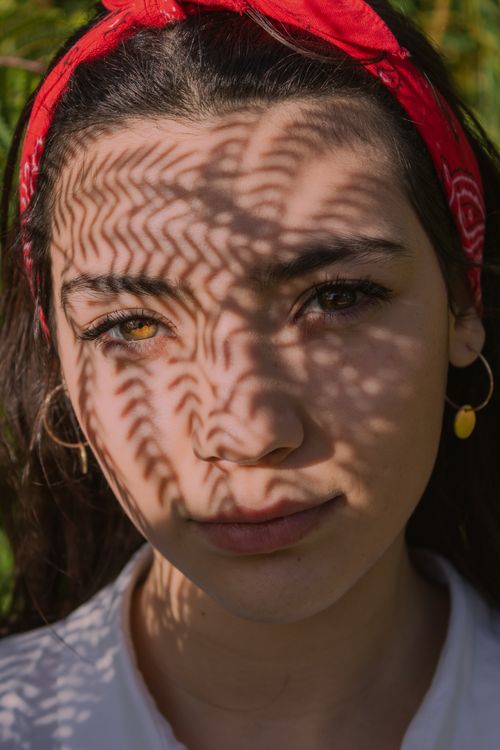 Free Close-up portrait of a woman with intricate leaf shadows on her face, wearing a red bandana. Stock Photo