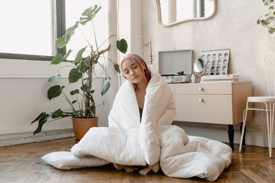 How Weighted Blankets Reduce Anxiety and Improve Sleep Quality A woman with pink hair wrapped in a blanket sitting on the floor in a stylish room.