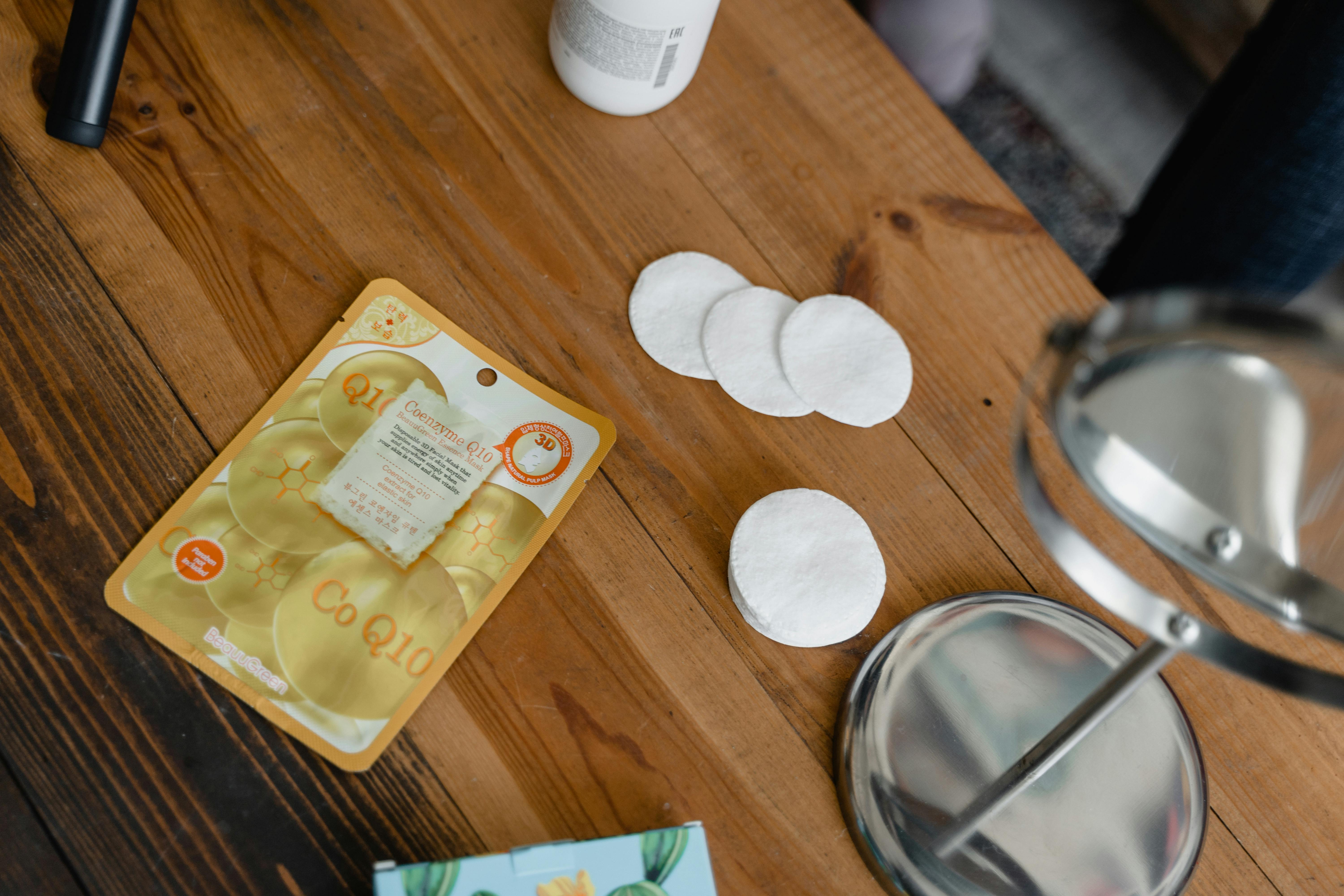 Beauty products and cotton pads arranged on a wooden table for skincare routines.