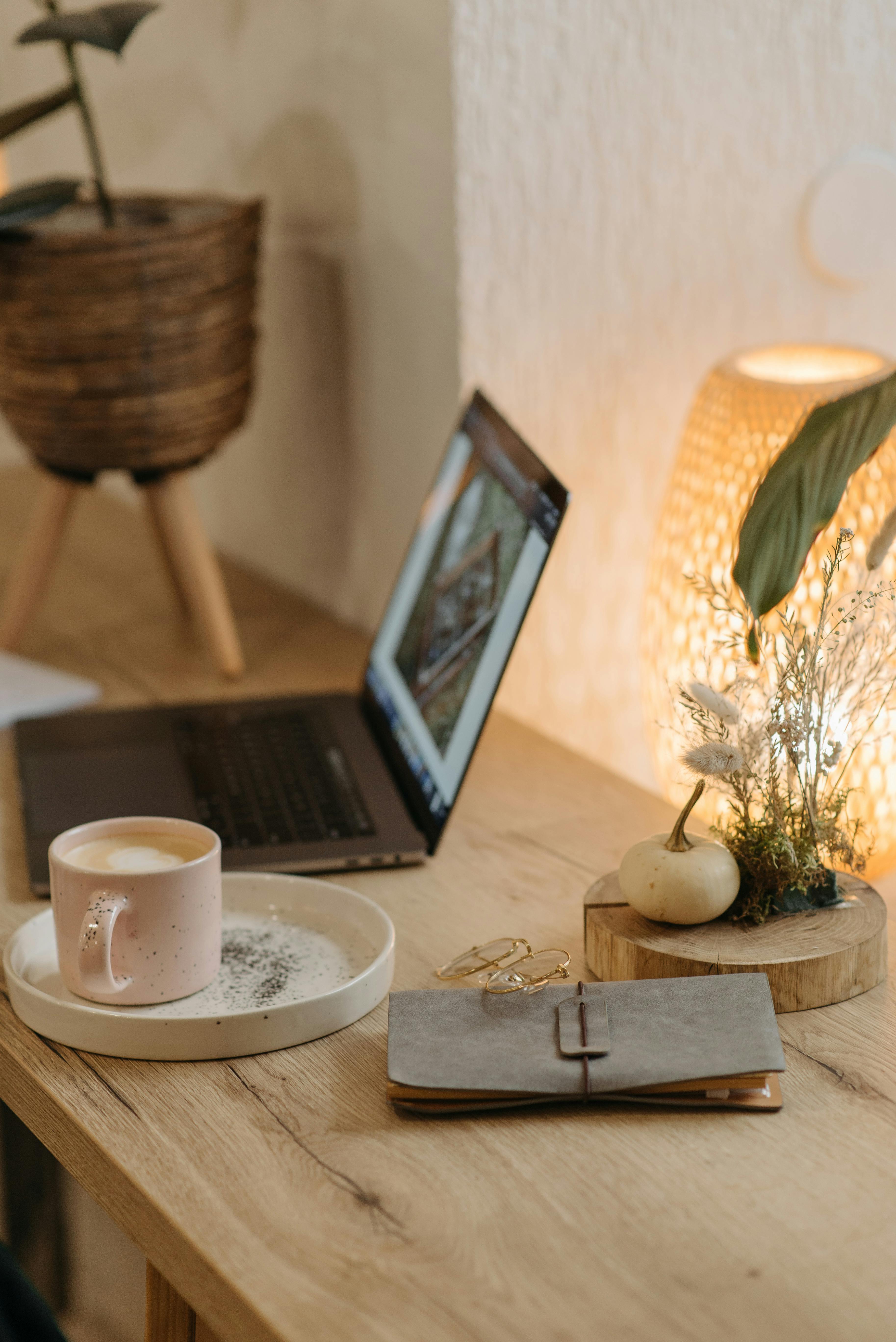 Free Warm and inviting workspace featuring a coffee cup, laptop, and decor on a wooden table. Stock Photo