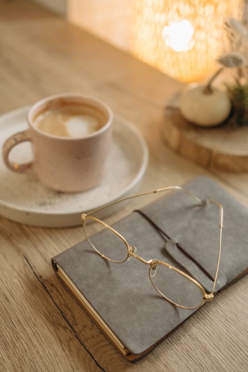 Free Warm cozy scene featuring a latte, notebook, and eyeglasses on a wooden table. Stock Photo