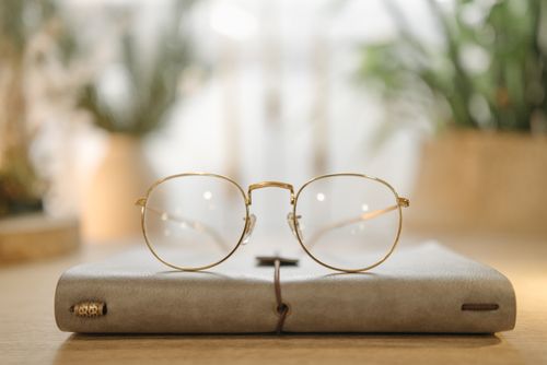 Free Close-up of stylish glasses on a leather notebook with soft light and plants in the background. Stock Photo