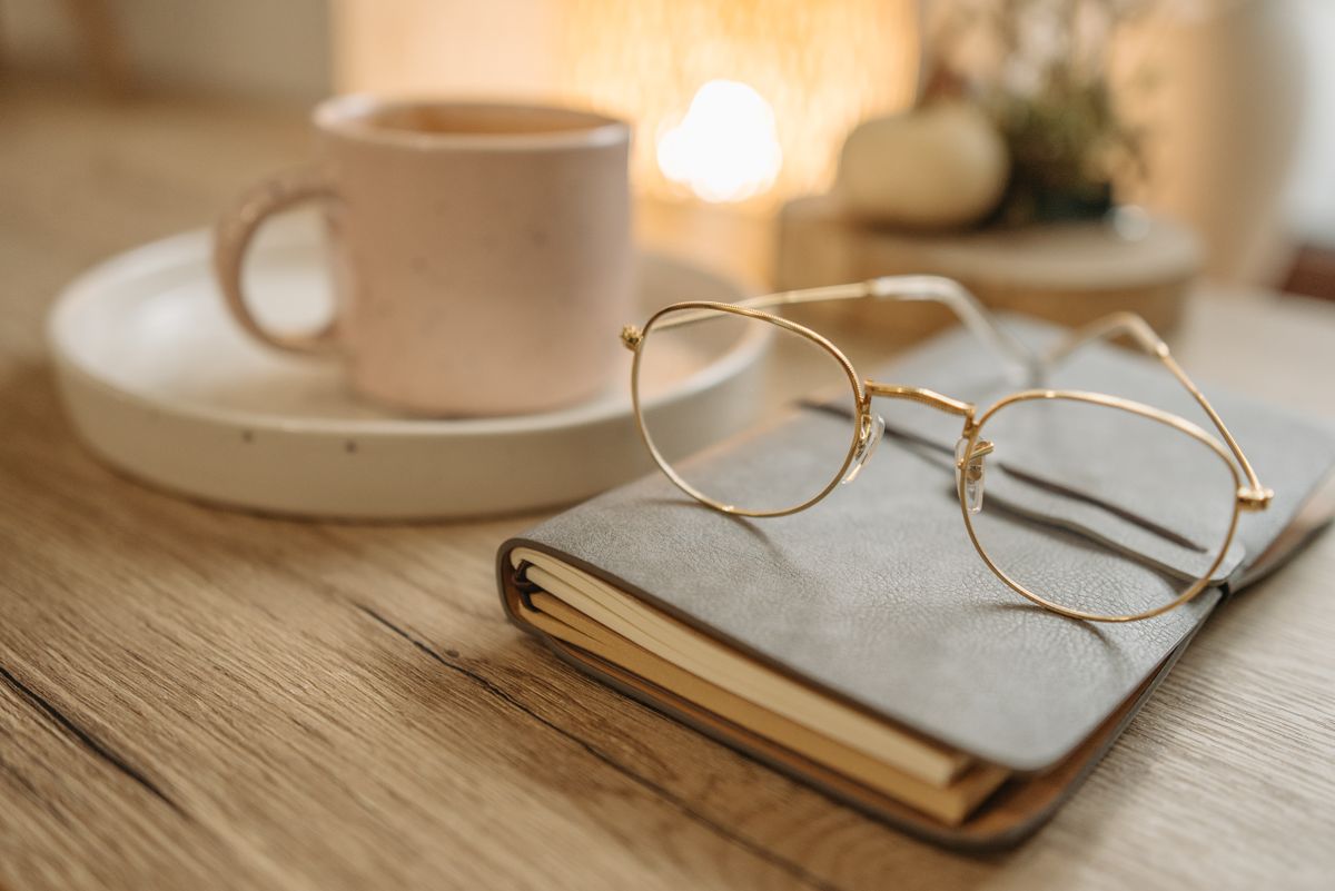 Lunettes posées sur un carnet fermé à côté d'une tasse de café sur un bureau en bois