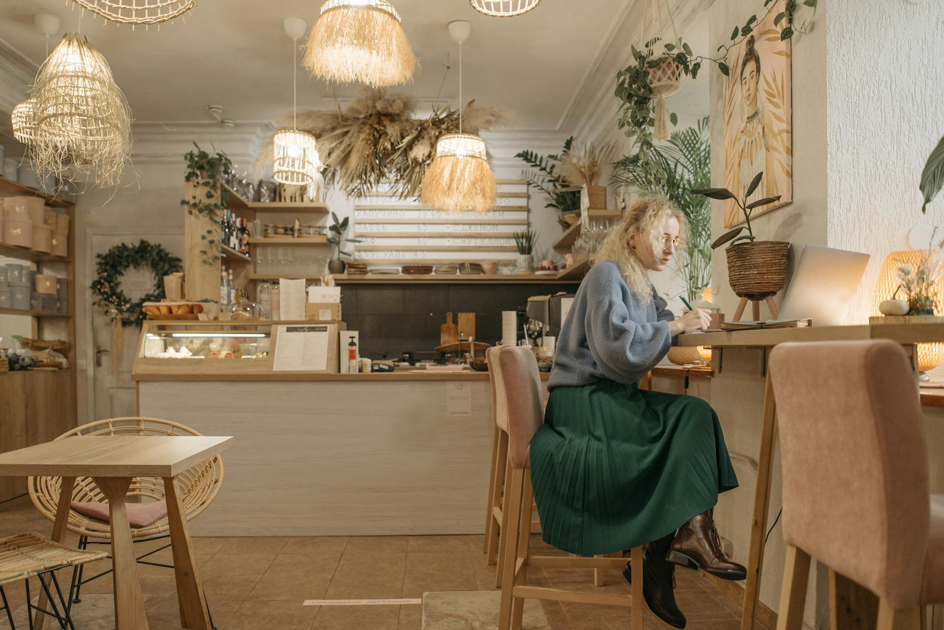 A young woman writing in a cozy coffee shop interior with warm lighting.