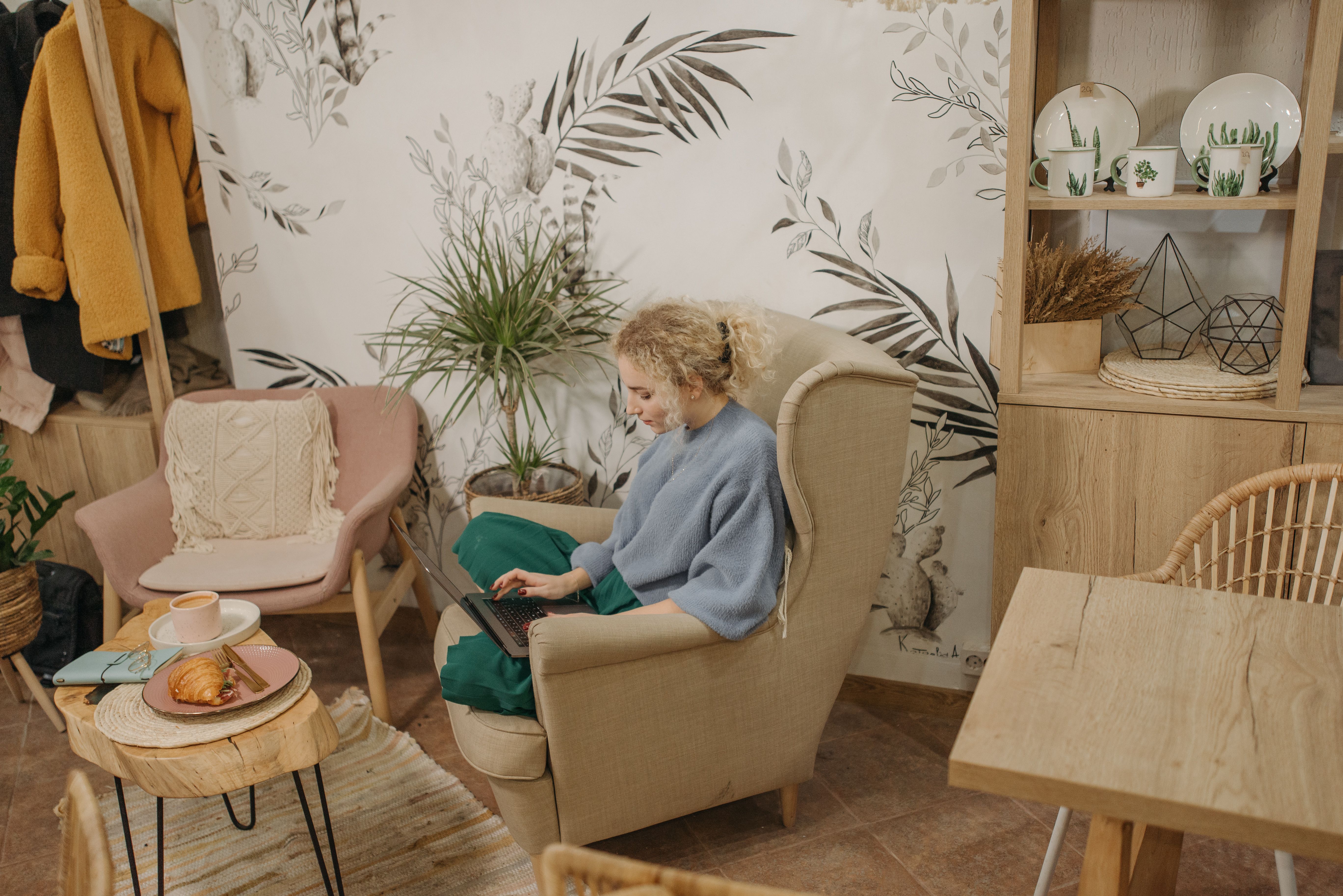 A woman working remotely in a cozy home setting with coffee and croissant.