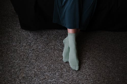 Free From above of crop anonymous female in socks sitting with crossed legs on carpet in house Stock Photo