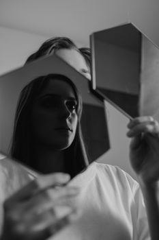 Black and white photo of a woman holding geometric mirrors, reflecting her face.