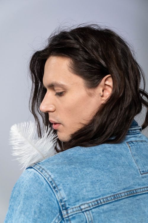 Free Caucasian man with long hair in denim jacket, holding a feather. Stock Photo
