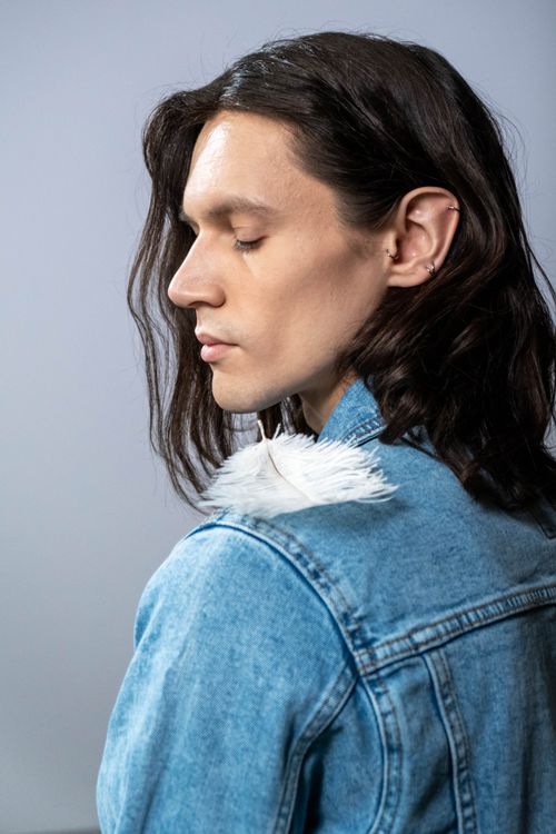 Free Portrait of an individual with long hair wearing a denim jacket and feather accessory. Stock Photo