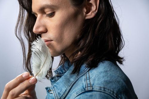 Free Profile view of an adult with long hair holding a delicate feather, set in a calm studio environment. Stock Photo