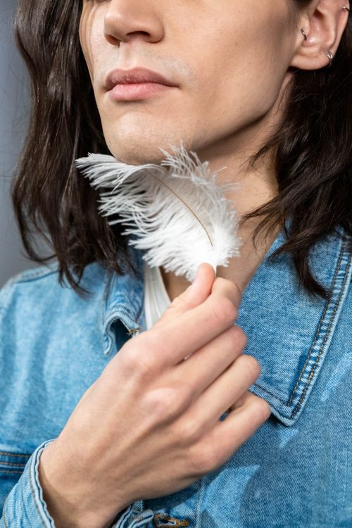 Free A person with long hair gently touches a white feather wearing a denim jacket. Stock Photo