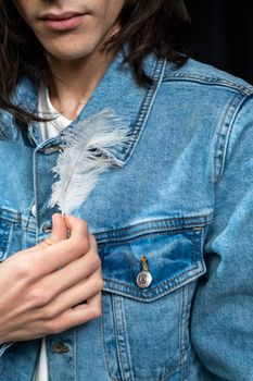 Close-up of a person holding a feather wearing a stylish denim jacket.
