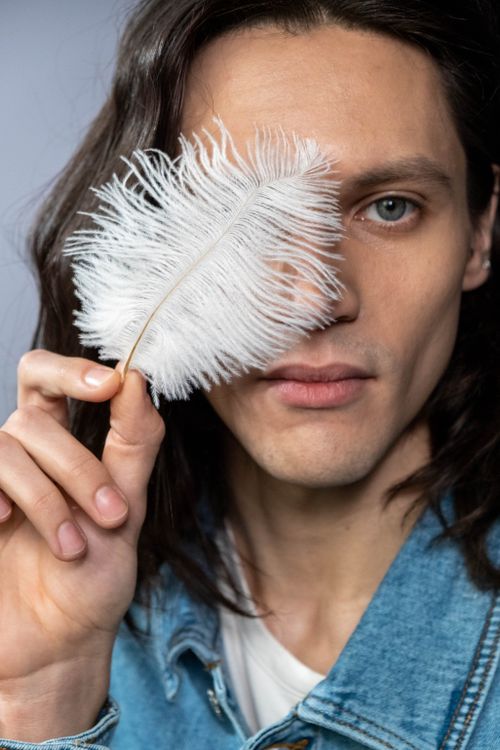 Free A portrait of a man with long hair holding a white feather, posing in a studio setting. Stock Photo