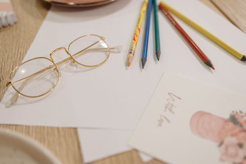 Free A cozy workspace featuring colored pencils, eyeglasses, and stationery set on a wooden table. Stock Photo